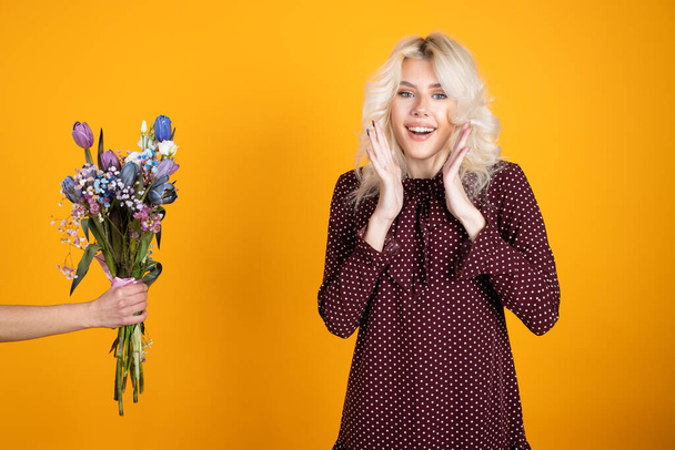 Excited blonde girl posing near tulip bouquet isolated on yellow background - Photo, Image
