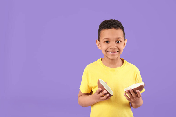 Χαριτωμένο Αφρο-αμερικανικό αγόρι με γλυκό αυγό σοκολάτας στο φόντο χρώμα - Φωτογραφία, εικόνα