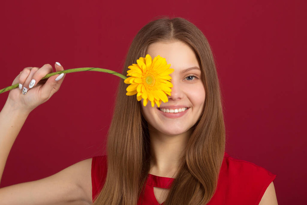 beautiful young woman with a flower in her hands on a red background - Fotografie, Obrázek