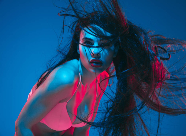 Attractive brunette model on blue studio background in neon light - Photo, image