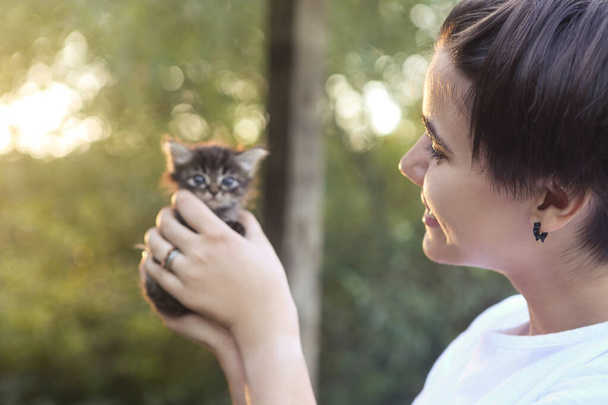Вид збоку весела дівчинка-підліток тримає чарівного маленького кошеня в руках у природі
 - Фото, зображення