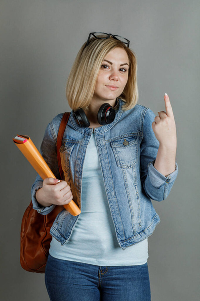 Μια όμορφη μαθήτρια, με ένα σακίδιο και ένα βιβλίο, δείχνει ένα χέρι από 1 έως 5 σε ένα γκρι φόντο. Η δευτεροβάθμια εκπαίδευση είναι η έννοια του University College - Φωτογραφία, εικόνα