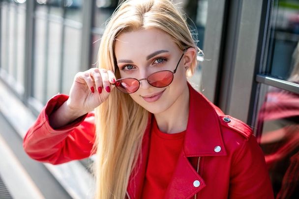 Closeup selfie-portrait student of attractive girl in sunglasses with long hairstyle and snow-white smile in city.happy blonde wearing red leather jacket. - Φωτογραφία, εικόνα