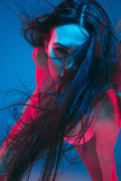 Attractive brunette model on blue studio background in neon light - Фото, зображення