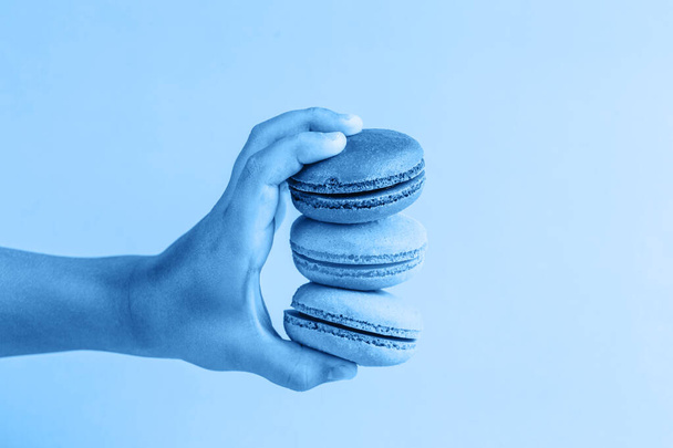 Colorful macaroons in a child's hand on a classic blue background, close-up, Flatley with copy space. Dessert with melon, lemon and raspberry flavor. Art - Foto, imagen