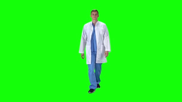 Hombre médico en bata blanca va y mirando hacia adelante sobre un fondo verde. Movimiento lento
. - Metraje, vídeo