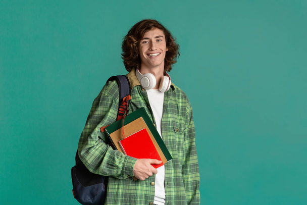 Onderwijsconcept. Vrolijke jongeman met rugzak en notitieboekjes over kleur achtergrond, lege ruimte - Foto, afbeelding