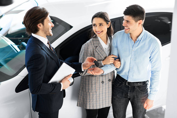 Couple Taking Key From Salesman In Auto Showroom - Photo, Image