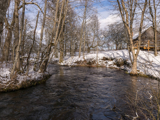paysage hivernal avec rivière sauvage à écoulement rapide, terre enneigée, beaucoup d'arbustes et de branches
 - Photo, image
