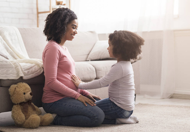 Pieni tytär koskettaa raskaana olevia äitejä vatsa leikkiessään yhdessä kotona
 - Valokuva, kuva