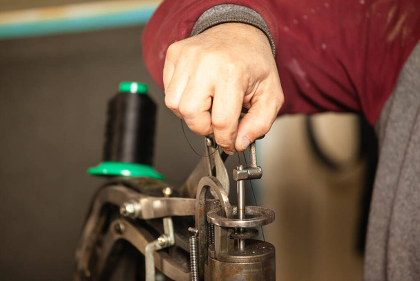 крупным планом руки сапожника вставляют нитку в швейную машинку
 - Фото, изображение
