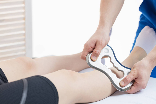 The doctor makes a massage with the Blade tool. Increased mobility of the soft tissues of the leg. White background, isolate - 写真・画像