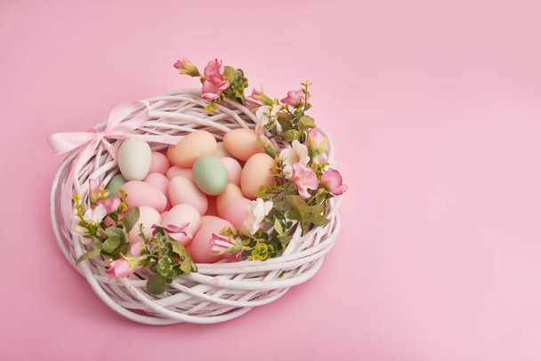 Colorful easter eggs in nest on pastel color background with flowers, copy space. Easter decorations. Easter background with painted eggs in nest, vintage style, top view. Spring greeting card. - Photo, Image