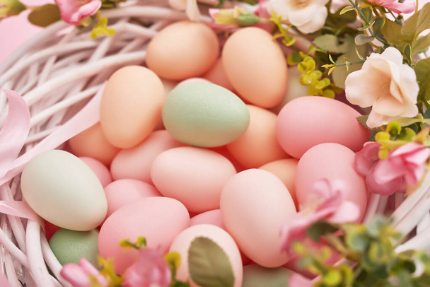 Le uova pasquali variopinte in nido su sfondo a colori pastello con fiori, copiano lo spazio. Decorazioni pasquali. Sfondo pasquale con uova dipinte a nido, stile vintage, vista dall'alto. Biglietto di auguri primavera
. - Foto, immagini