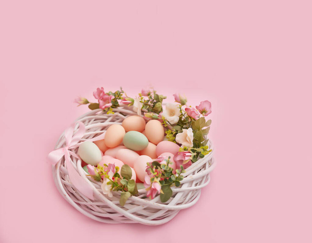 Huevos de Pascua coloridos en el nido sobre fondo de color pastel con flores, espacio de copia. Decoraciones de Pascua. Fondo de Pascua con huevos pintados en nido, estilo vintage, vista superior. Tarjeta de felicitación de primavera
. - Foto, imagen