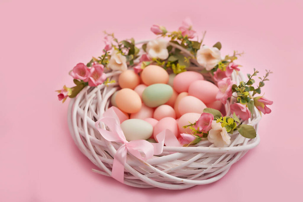 Colorful easter eggs in nest on pastel color background with flowers, copy space. Easter decorations. Easter background with painted eggs in nest, vintage style, top view. Spring greeting card. - Photo, Image