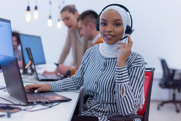 Γυναικεία εξυπηρέτηση πελατών Εκπρόσωπος Απάντηση Ερωτήσεις πελάτη σε ένα σετ ακουστικών. Πολυεθνική Ομάδα Ειδικών. Χαρούμενη Αφρικανή μουσουλμάνα στο τηλεφωνικό κέντρο.. - Φωτογραφία, εικόνα