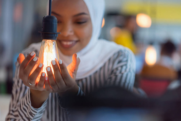 Beautiful african muslim woman holds modern lamp bulb with smiling happy expression, idea concept with selective focus. - Fotografie, Obrázek
