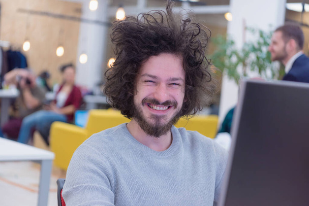 Jonge mannelijke web developer glimlachen op het werk, terwijl de Groep van een jong bedrijf multi-etnische mensen brainstormen en bespreken business plan op vergadering op zonnig helder kantoor interieur. - Foto, afbeelding