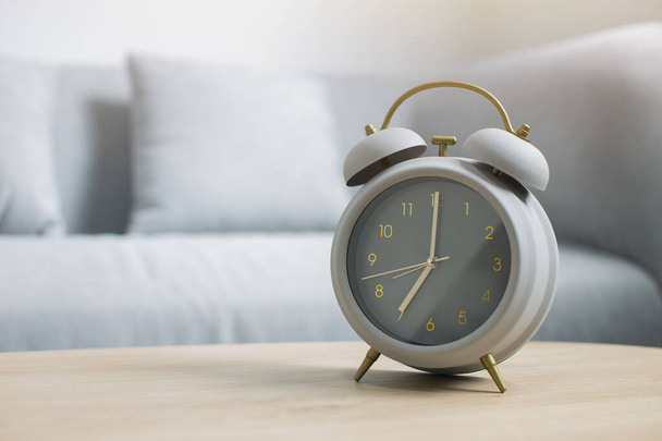 Reloj despertador gris en una mesa de madera en la luz de la mañana en la sala de estar, concepto de buenos días
 - Foto, imagen