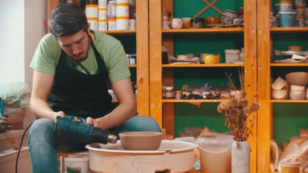 Pottery - master in green t-shirt is drying a clay bowl with a construction hairdryer - Footage, Video