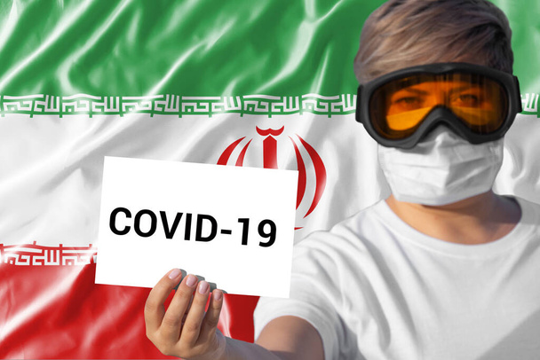 Γυναίκα με μάσκα προσώπου φύλλο συγκράτησης με επιγραφή Covid-19 κατά της ιρανικής σημαίας. Έννοια της προσοχής για την εξάπλωση του κινεζικού ιού Coronavirus Covid-19 Novel Coronavirus Πνευμονία ιός σε όλο τον κόσμο - Φωτογραφία, εικόνα