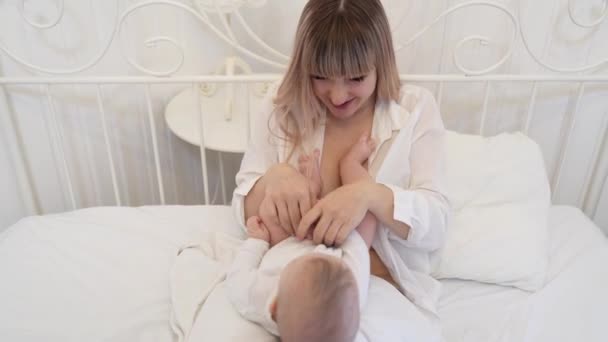 mother kissing baby feet lying on bed in bedroom - Video