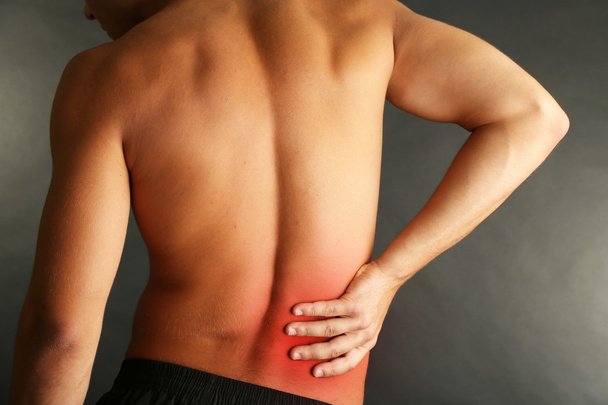 junger Mann mit Rückenschmerzen auf grauem Hintergrund - Foto, Bild