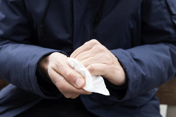 lähikuva valkoihoisesta miehestä kadulla desinfioimassa käsiään märällä pyyhkeellä
 - Valokuva, kuva