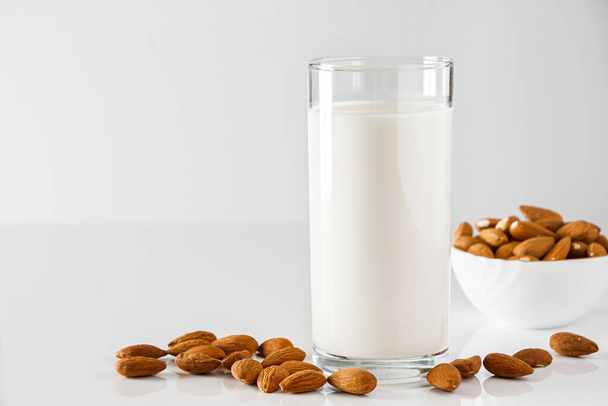 A glass of almond milk on a white background. Lactose-free vegetable diet milk. Gluten free almond drink on a blue background. Super Food - A glass of almond milk for a healthy diet. Trending food, vertical photo. Place for your text. - Foto, Imagen