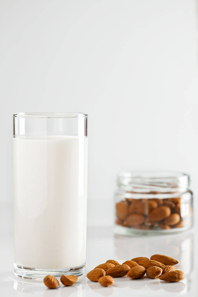 Ein Glas Mandelmilch auf weißem Hintergrund. Laktosefreie pflanzliche Diät-Milch. Glutenfreies Mandelgetränk auf blauem Hintergrund. Super Food - Ein Glas Mandelmilch für eine gesunde Ernährung. Trending food, vertikales Foto. Platz für Ihren Text. - Foto, Bild