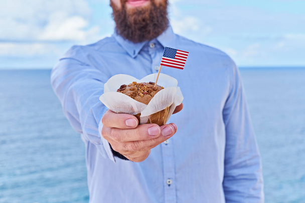 Hombre sin cabeza sostiene cupcake con la bandera americana miniatura EE.UU.. Tarjeta de felicitación para la celebración del Día del Presidente en América concepto, Día de la Independencia, Día de la Bandera EE.UU., efecto de gran angular
 - Foto, imagen