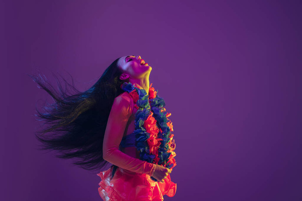 Attractive hawaiian brunette model on purple studio background in neon light - Фото, изображение