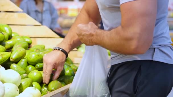 Pretty Strong Healthy Man Buys Food, Fruits, Avocados, is Making Purchases in the Supermarket, Choosing Products at the Supermarket for Cooking, Healthy Foods, Tomatoes, Avocados, Fruits, Oranges at - Felvétel, videó
