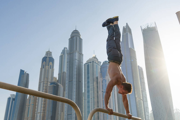 Muscular man doing workout on the street with cityscape of skyscrapers on background in Dubai. Concept of healthy lifestyle and modern - Foto, Imagem