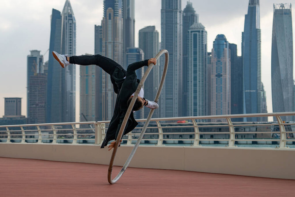 Cyr Wheel artist wearing black and white smart clothes with cityscape background of Dubai during sunset - Fotoğraf, Görsel