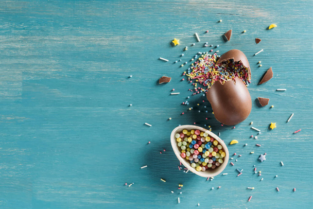 top view of chocolate egg with Easter sprinkles on blue wooden table - Vector, Image