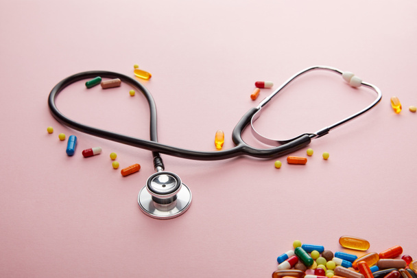 High angle view of stethoscope and bright colorful medicines on pink  - Photo, Image