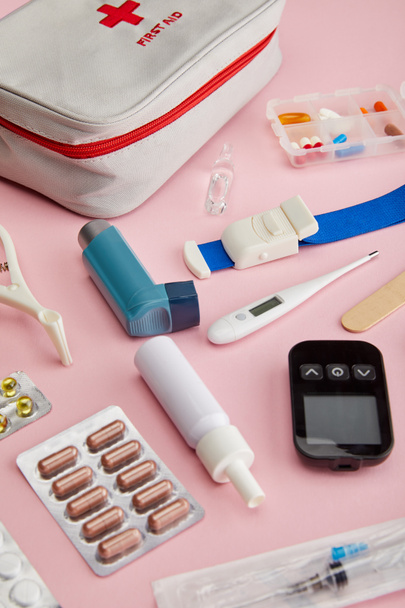 Hoge hoek weergave van EHBO-kit in de buurt van medische objecten op roze achtergrond - Foto, afbeelding
