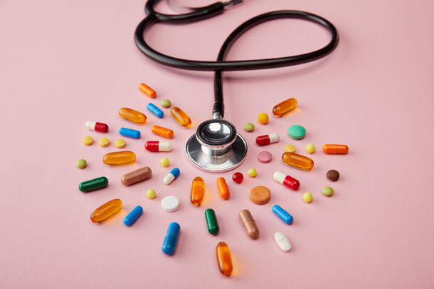 Hoge hoek uitzicht op stethoscoop in de buurt heldere kleurrijke pillen op roze - Foto, afbeelding