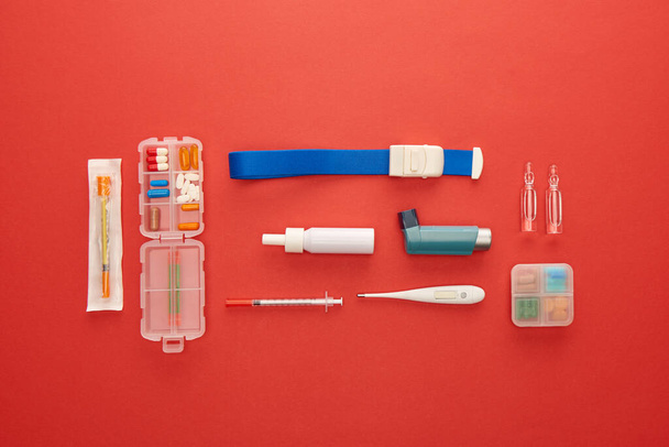 Tasainen makasi lääkkeiden ja lääketieteellisten esineiden kanssa punaisella taustalla
 - Valokuva, kuva