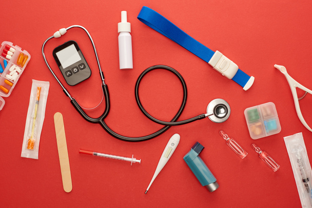 Vista superior do estetoscópio, inalador de asma, medicamentos e objetos médicos em fundo vermelho
 - Foto, Imagem