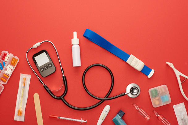 Top view sztetoszkóp, gyógyszerek és orvosi tárgyak piros alapon - Fotó, kép