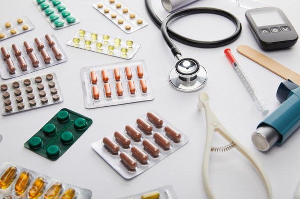 Korkeakulmainen näkymä lääketieteellisistä esineistä ja lääkkeistä valkoisella taustalla
 - Valokuva, kuva