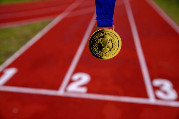 Gold medal, red running track in background, sport motivation concept photo. Original photo for summer olympic in Tokyo 2020 - Foto, Imagem