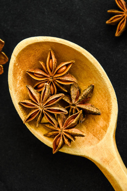wooden spoon with star anise on black background, christmas spices - Photo, Image