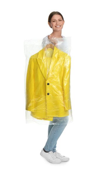 Young woman holding hanger with jacket in plastic bag on white background. Dry-cleaning service - Fotoğraf, Görsel