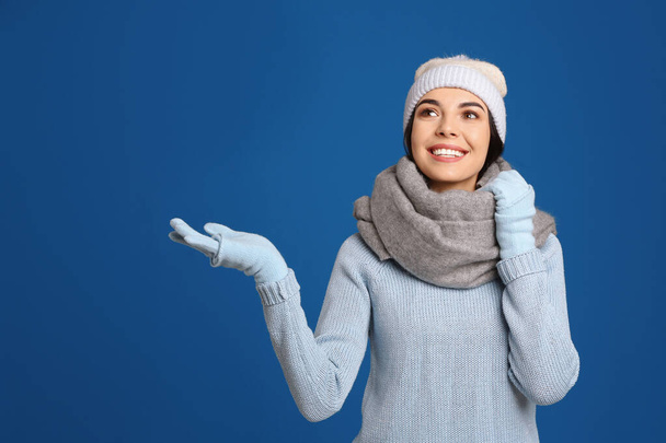 Young woman wearing warm sweater, gloves, scarf and hat on blue background. Winter season - Φωτογραφία, εικόνα