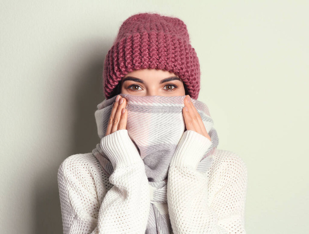 Young woman wearing warm sweater, scarf and hat on light background. Winter season - Foto, afbeelding