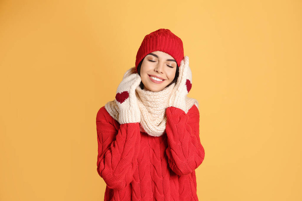 Young woman wearing warm sweater, scarf, mittens and hat on yellow background. Winter season - Φωτογραφία, εικόνα